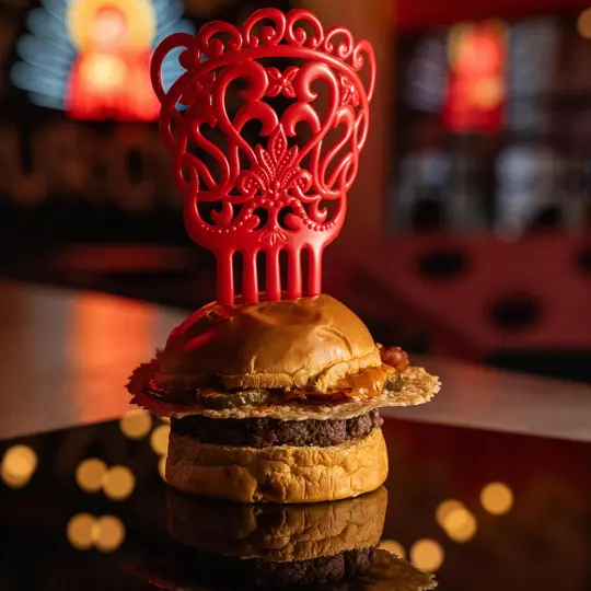 Hambúrguer em pão brioche dourado, coroado com uma peça vermelha esculpida